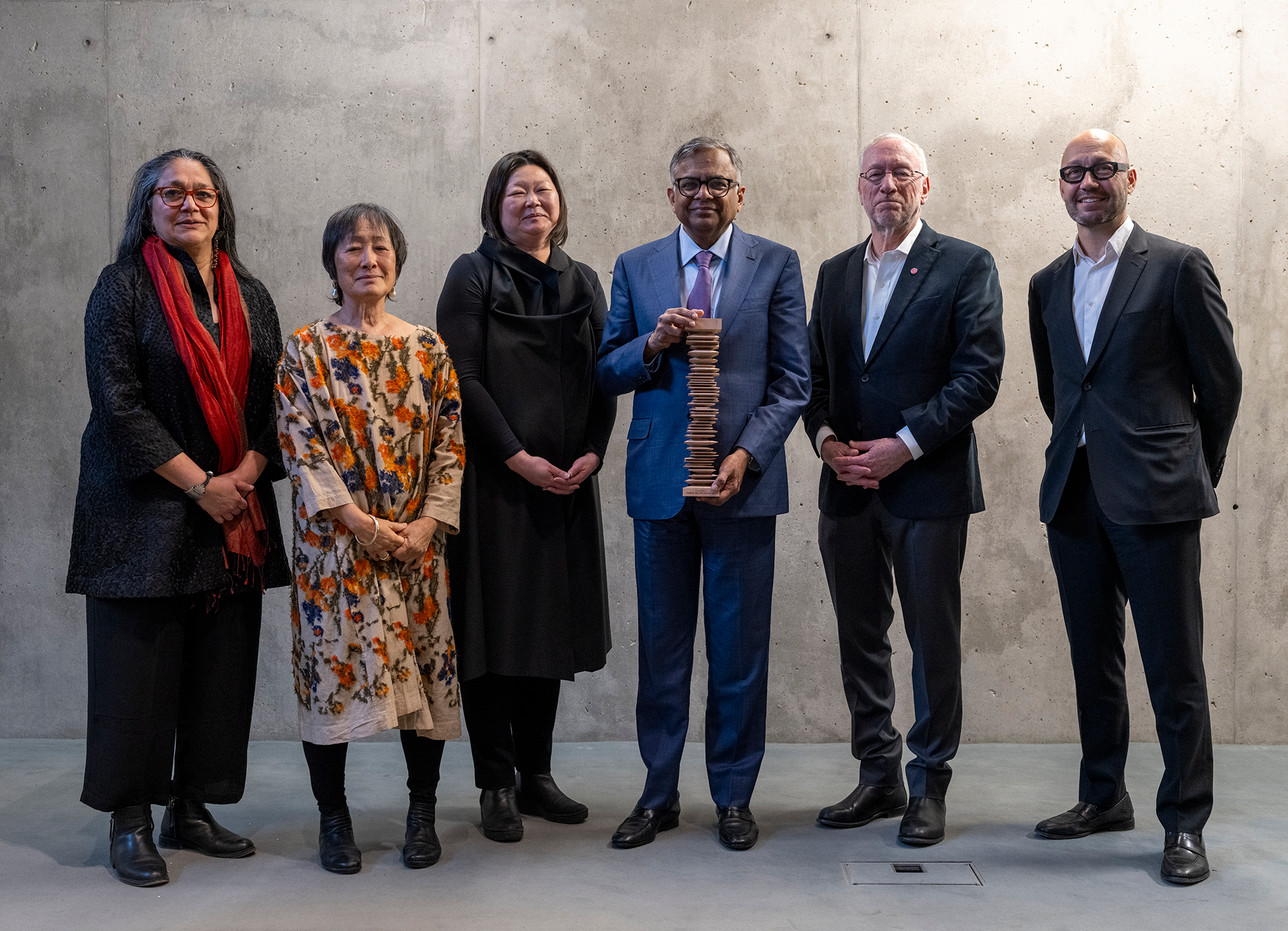 Row of formally dressed people, with the wooden award being held at center.