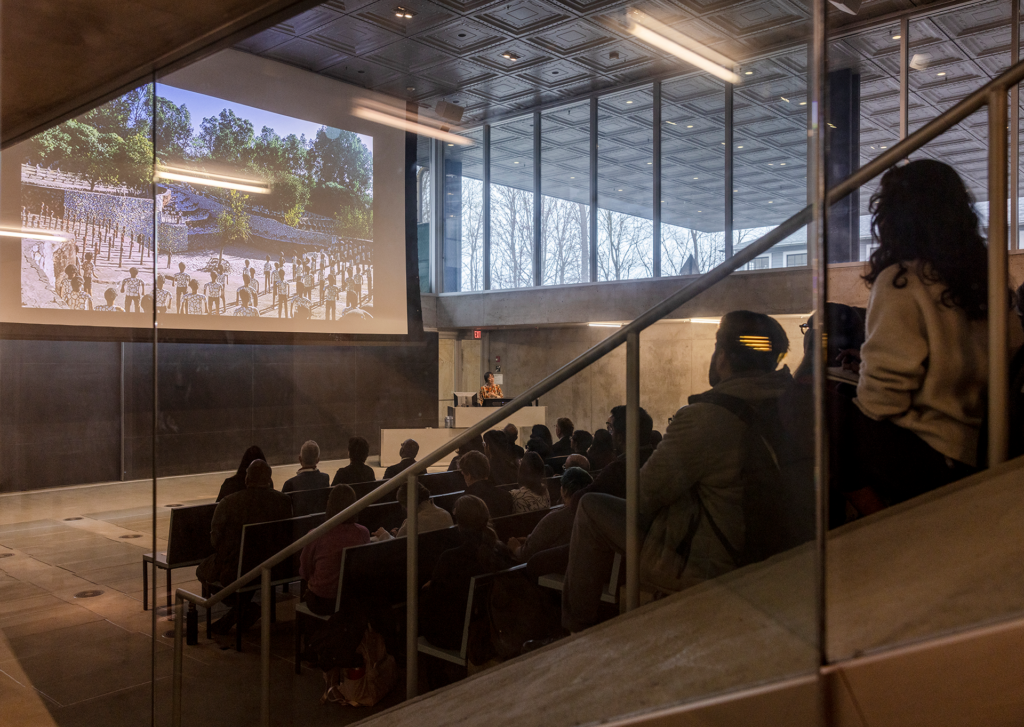 Crowd gathered in a lecture hall seated in front a screen projection