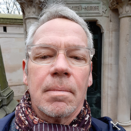 A man with short grey hair and clear framed glasses.