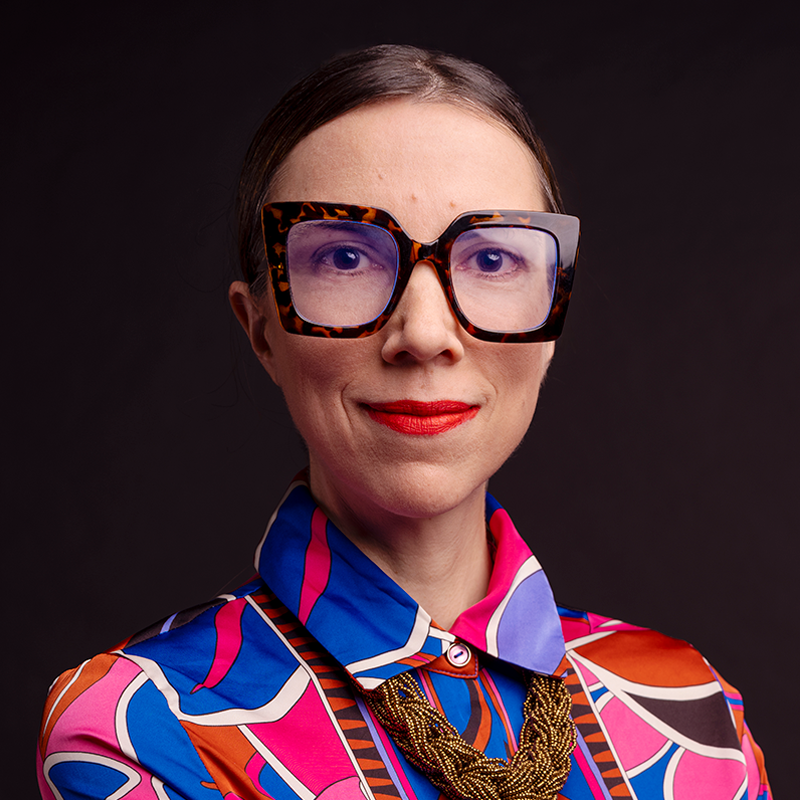 A person wearing large framed glasses and a brightly colored shirt.