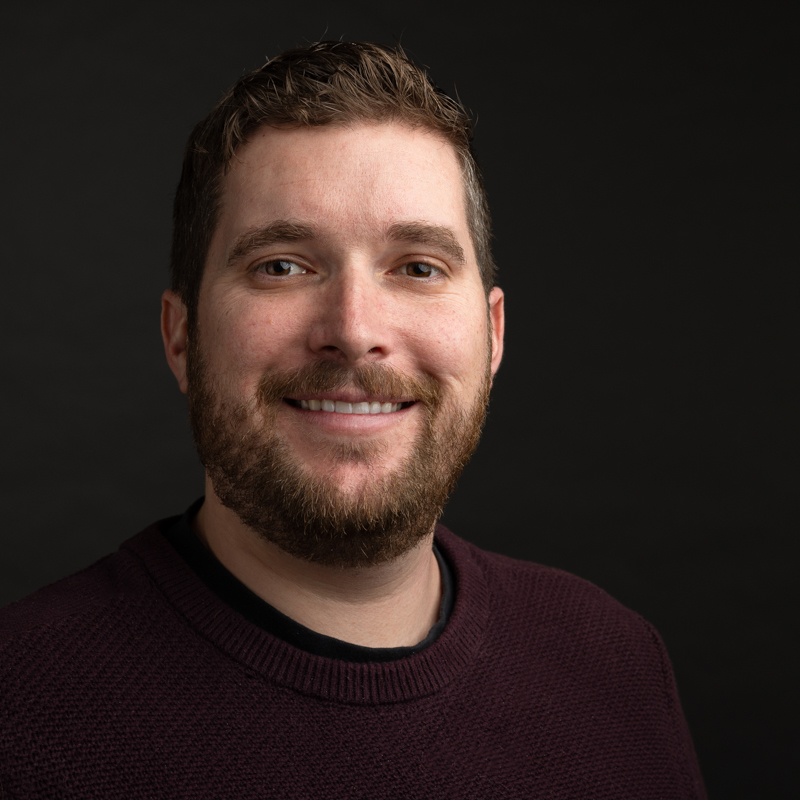 A man smiling with a maroon sweater on.