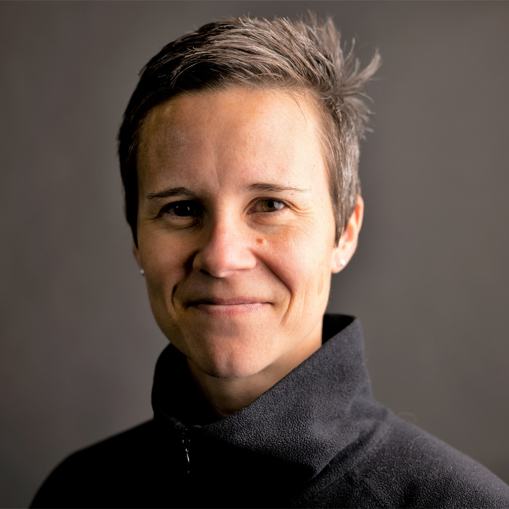 A person with short brown hair wearing a black turtle neck quarter-zip sweater.