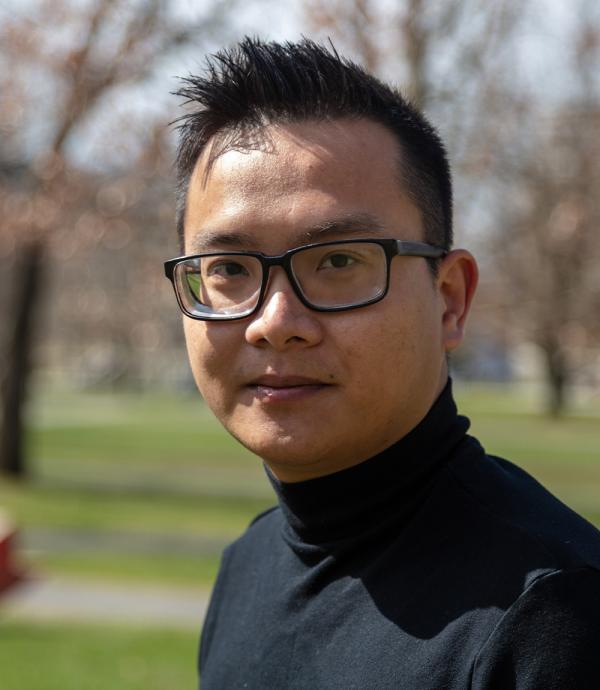 a young man with black spiky hair wearing a black turtle neck shirt and black framed glasses