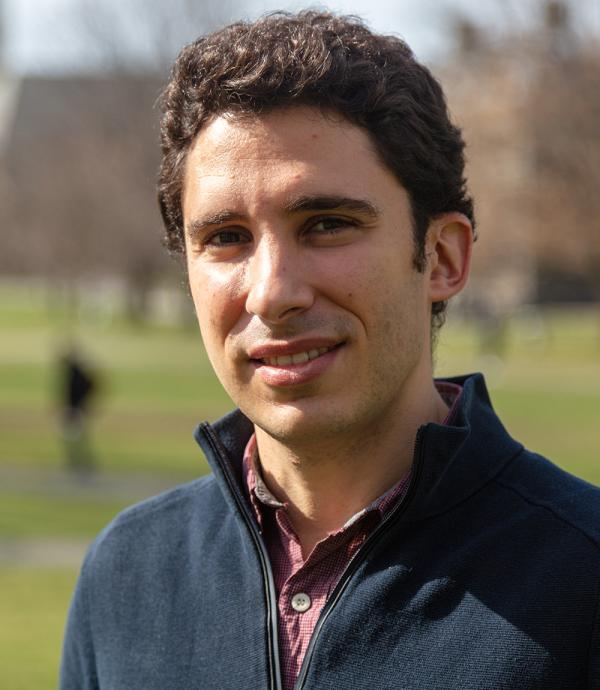 a man with curly short hair wearing a dark blue quarter zip and a red button down shirt