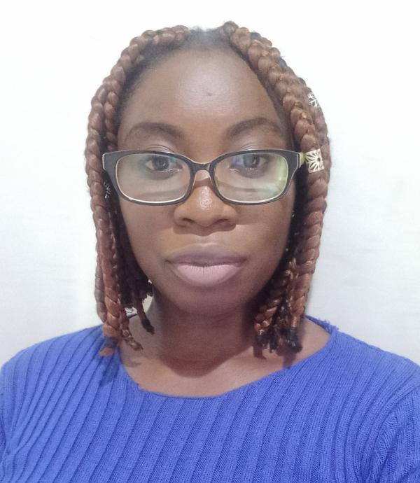 a person with braided hair, glasses, and a blue shirt in front of a white wall.