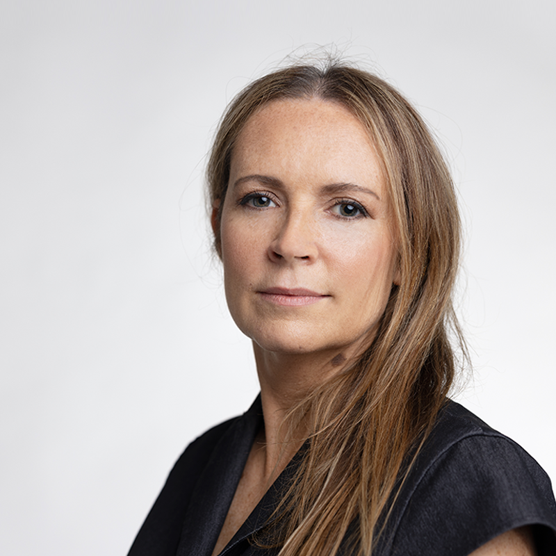 A person with long hair and a black shirt posing in front of a white background.