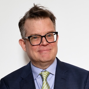 Man wearing glasses and a suit smiles at the camera.