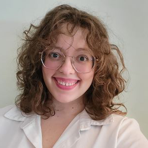 Person with shoulder length dark blonde hair. Wearing gold wire rimmed glasses and white blouse.