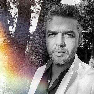 Black and white image of a man wearing a white blazer and dark colored button up shirt.