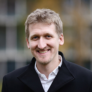 head and shoulders of a smiling man wearing a dark jacket over a white collared shirt