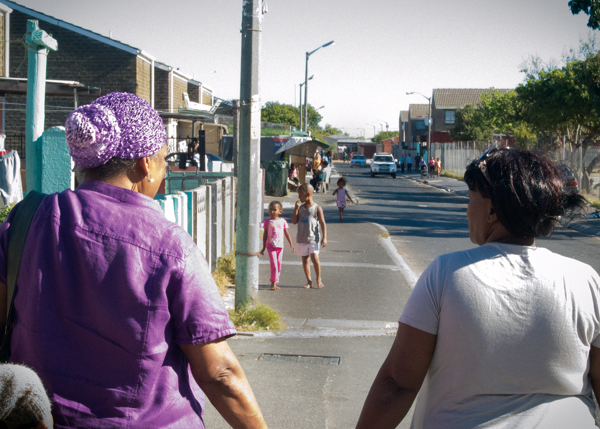 Women walking away from the camera along an urban street with children in the distance