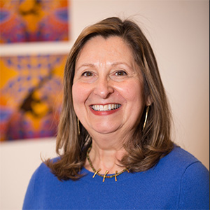 headshot of a woman with brown hair wearing a royal blue shirt and a necklace