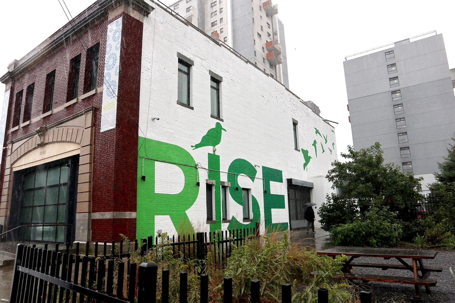 A person walking next to a building with the letters, R, I, S, E on it.