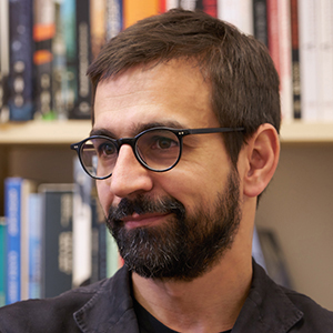 a man with glasses with book lined shelves in the background