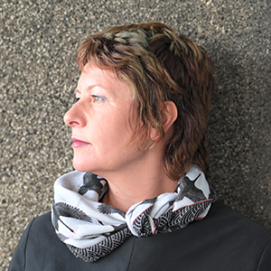 Woman with short brown hair wearing a grey top and white scarf looking off to the right