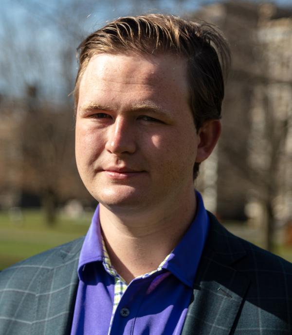 a young man with short blonde hair, wearing a purple dress shir with a pin striped suit jacket