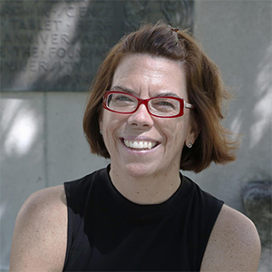 A person smiling with a black tank top and red glasses.