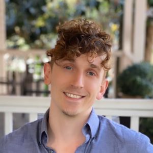 Person with brown curly hair wearing a blue button down shirt