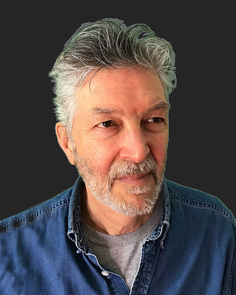 Person with blue jean shirt, grey beard, and grey hair