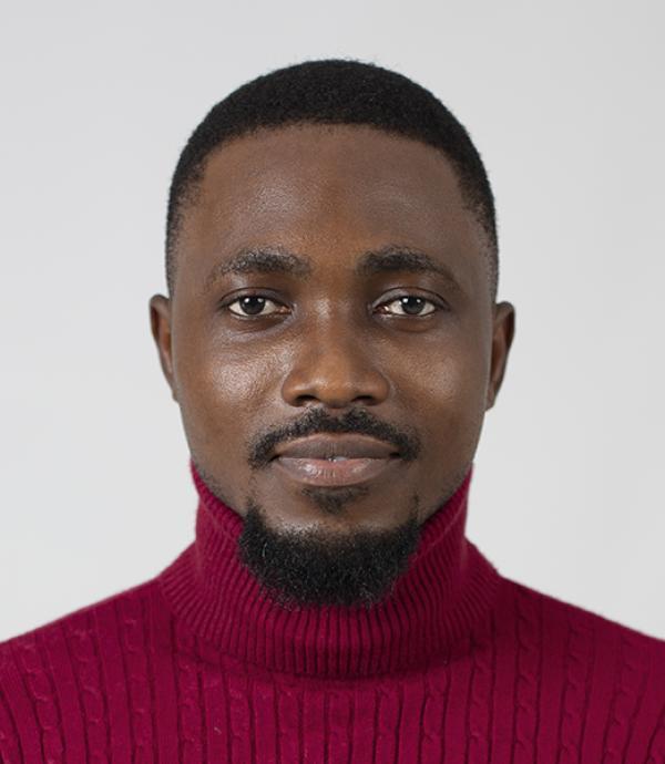 a person with a goatee wearing a bright burgundy colored turtle neck in front of a white wall