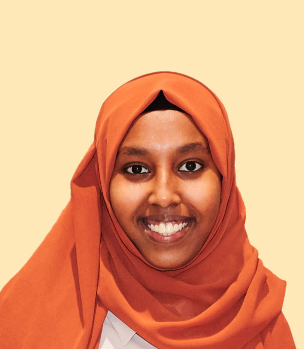 a person wearing an orange headdress and white shirt in front of a cream colored wall