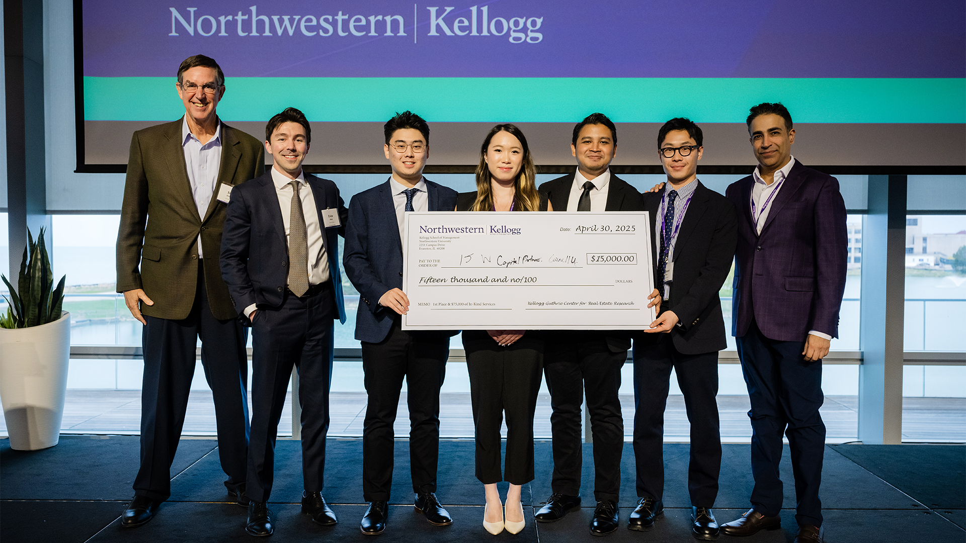 Students standing on stage holding a symbolic prize check