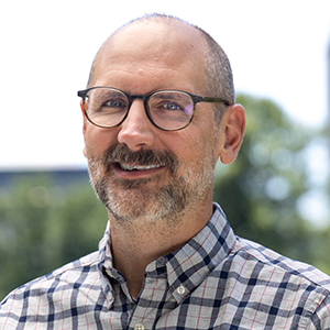 A person wearing a plaid button down a shirt and glasses.
