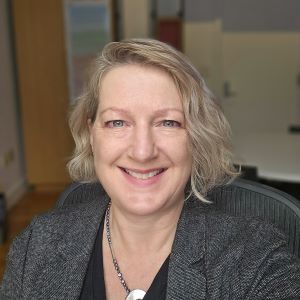 Selfie of person with chin-length blonde hair sitting in an office. She is smiling