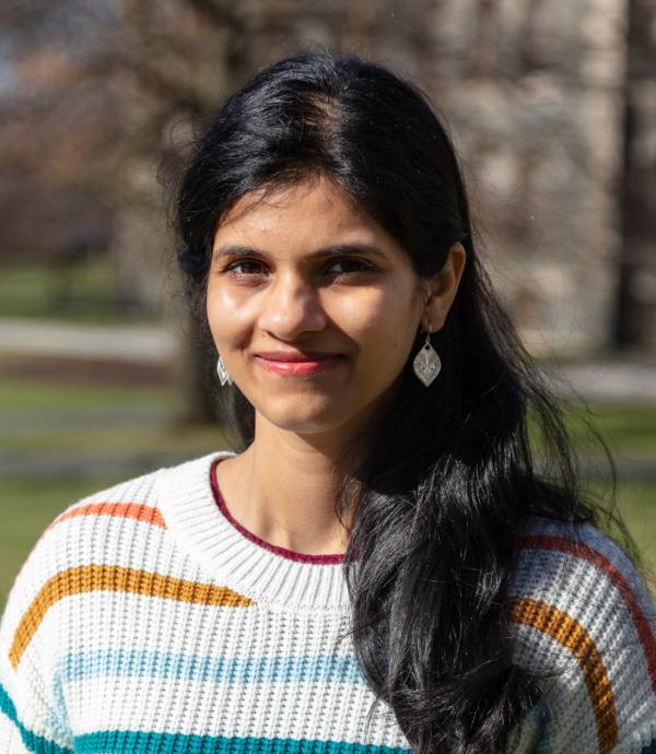 a woman with long black hair wearing silver earrings and a colorfully striped knitted white sweater