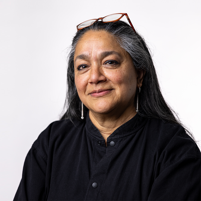 headshot of a woman with long dark hair wearing a black shirt and glasses resting on the top of her head
