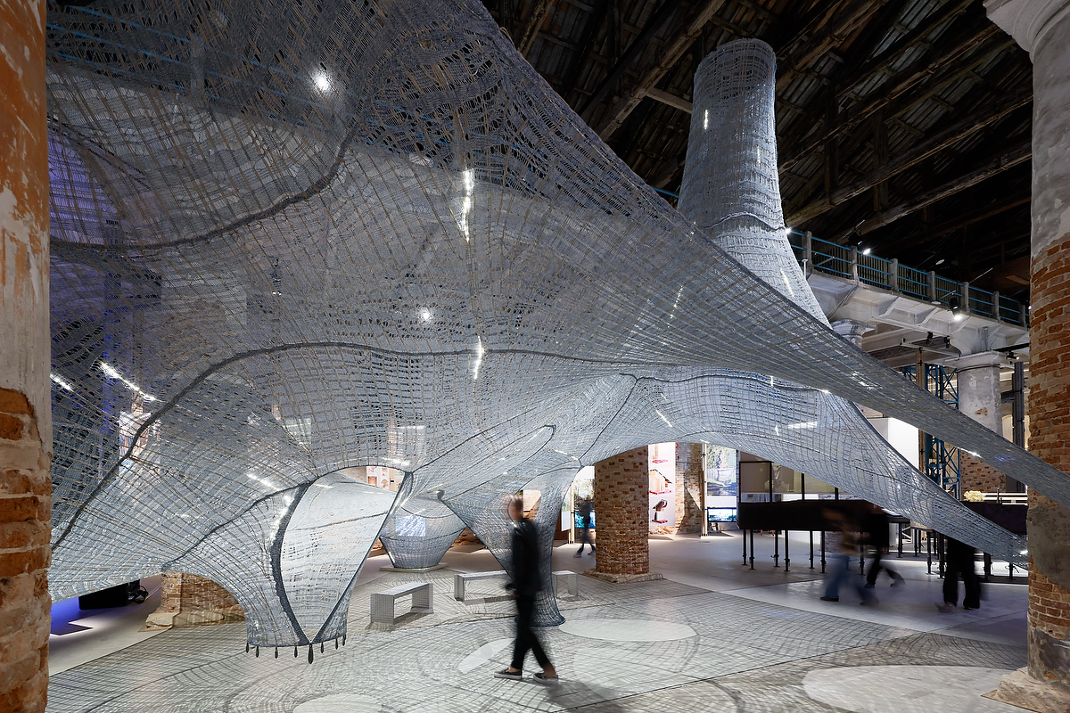Knitted natural fibers woven to create a structure hanging from the ceiling inside a brick-walled space