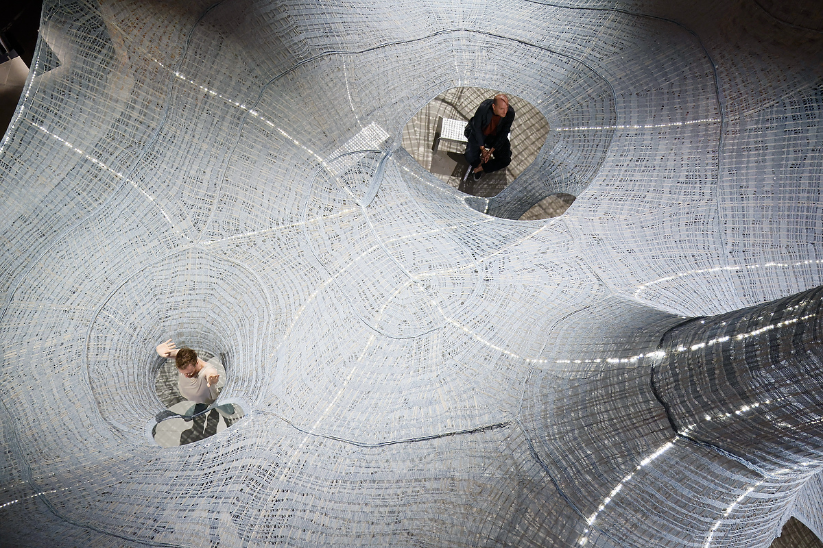 Knitted natural fibers woven to create a structure hanging from the ceiling inside a brick-walled space
