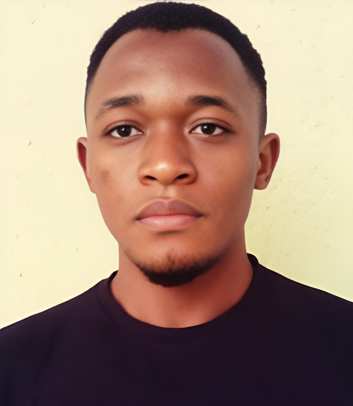 a young man with a goatee and a black shirt in front of a cream colored wall
