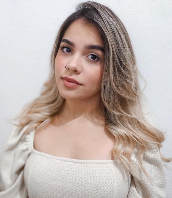 a young woman with blonde hair and a nose ring wearing a cream colored dress in front of a white wall