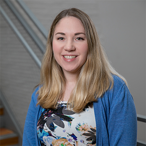 A woman with blonde hair and a white floral dress and a blue sweater.