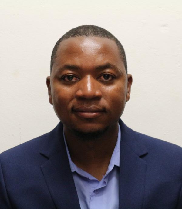 a man wearing a blue dress shirt and a dark blue blazer jacket in front of a white wall