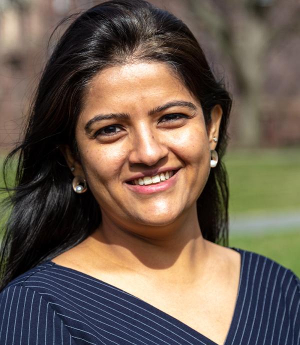 a young woman with long black hair wearing pearl earrings and smiling while outside wearing a blue and white striped dress shirt