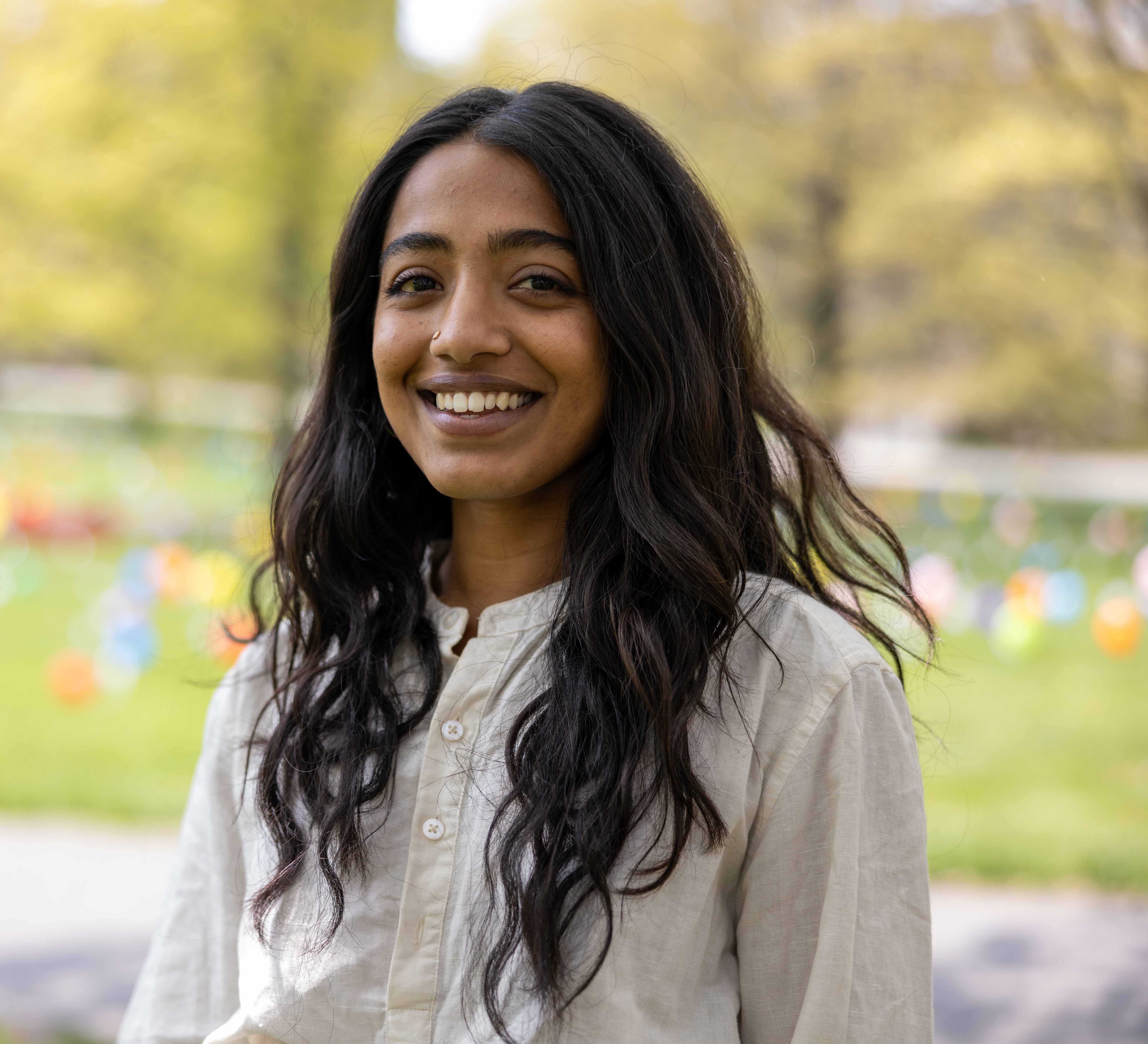 A person smiling with long black hair and a tan button down shirt.