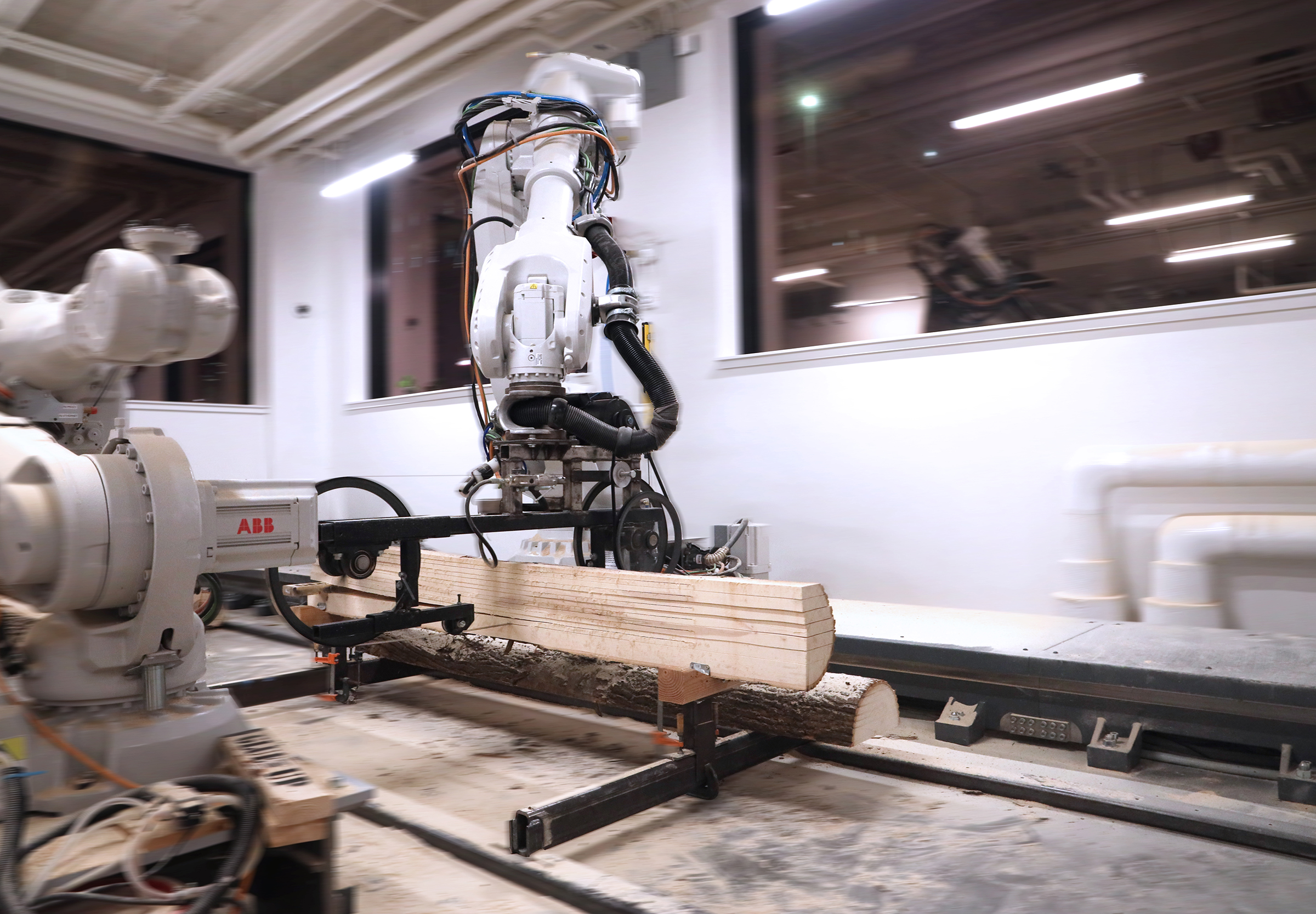 A large robotic arm handling a piece of wood in a white room with windows.