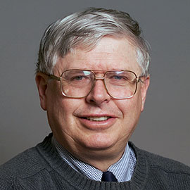 A person with grey hair and glasses wearing a tie