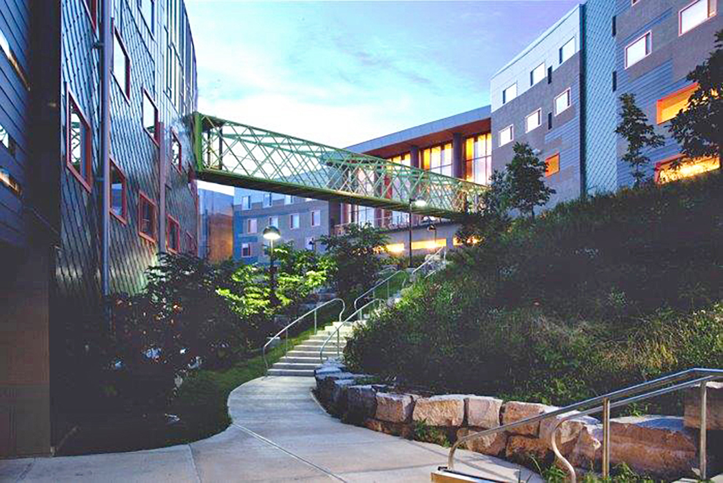 A skywalk bridge connects two buildings, crossing over stone stairs.