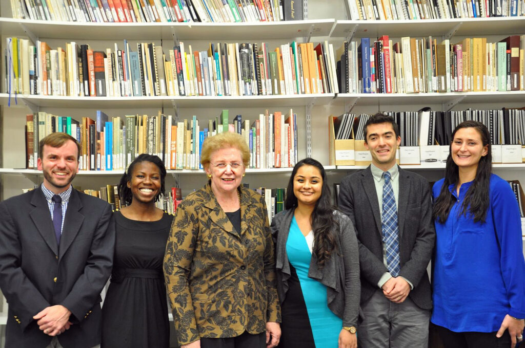 An older woman poses for a photo with five college students.