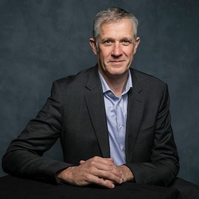 A person wearing a black jacket and a blue shirt with their hands folded.