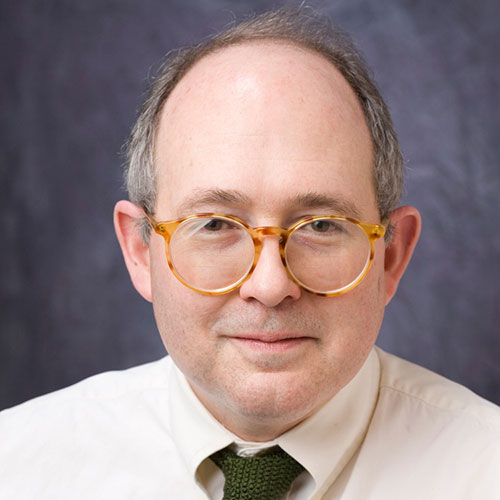 headshot of a man with tortoise shell glasses wearing a white shirt and green tie