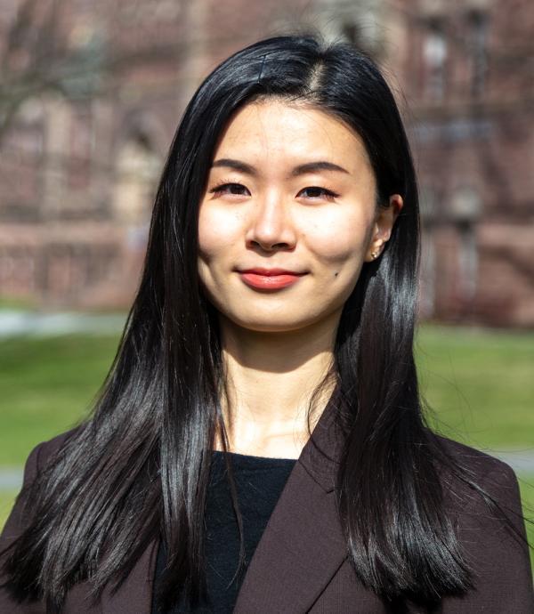 a young woman with long black hair wearing a black shirt with a dark gray suit jacket while standing outside
