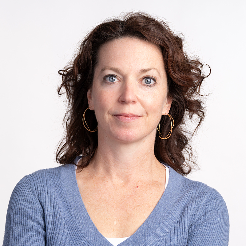 A person with wavy brown hair wearing a blue shirt over a white shirt