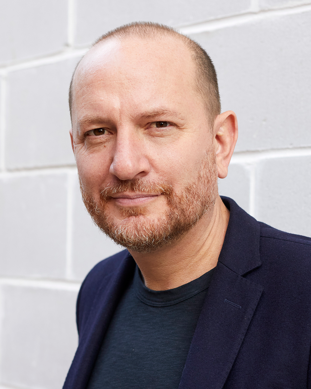 Man in a dark jacket standing against a grey brick wall