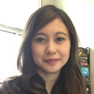 A person with brown hair smiling with books on a bookshelf in the background.