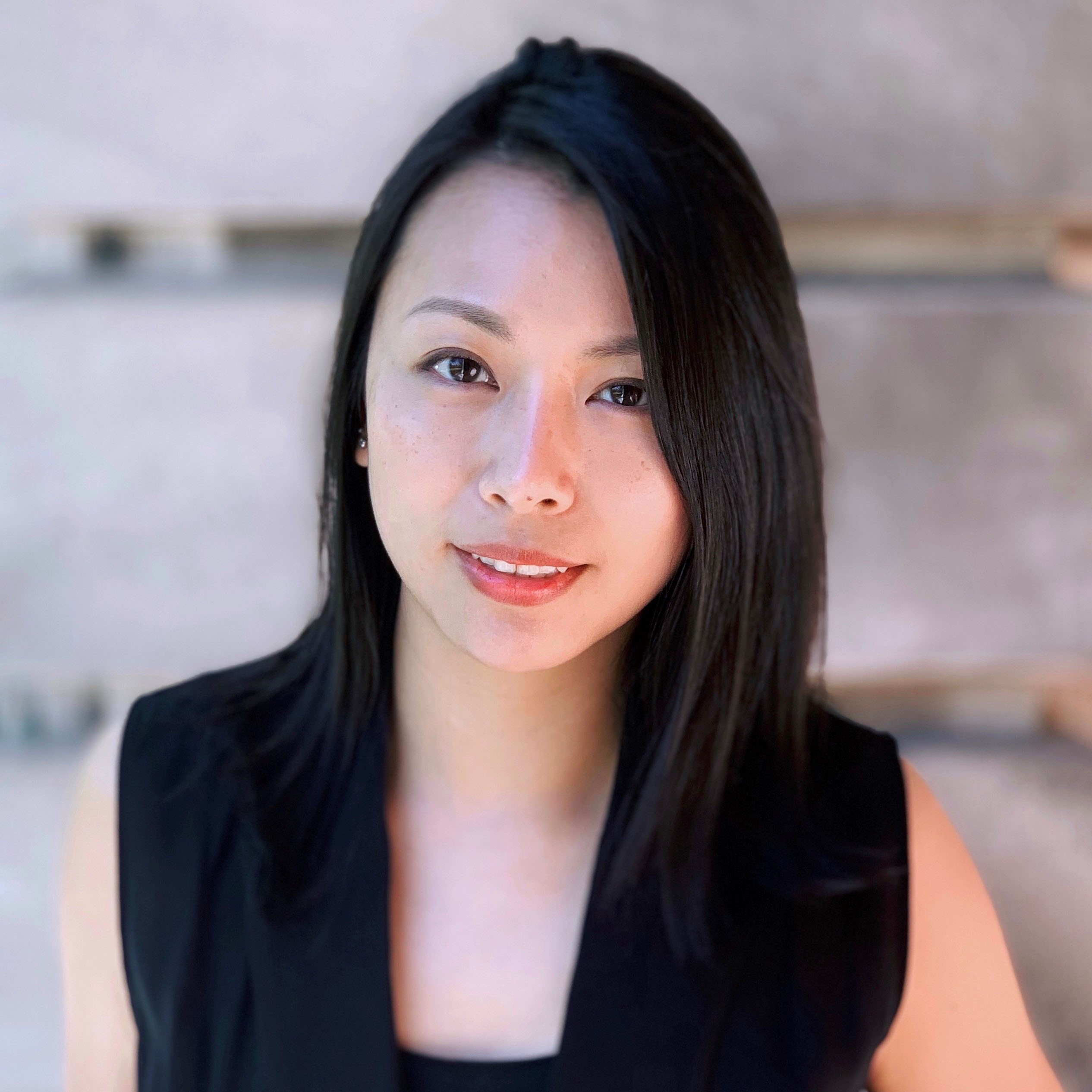 A woman with black hair standing in front of a concrete wall