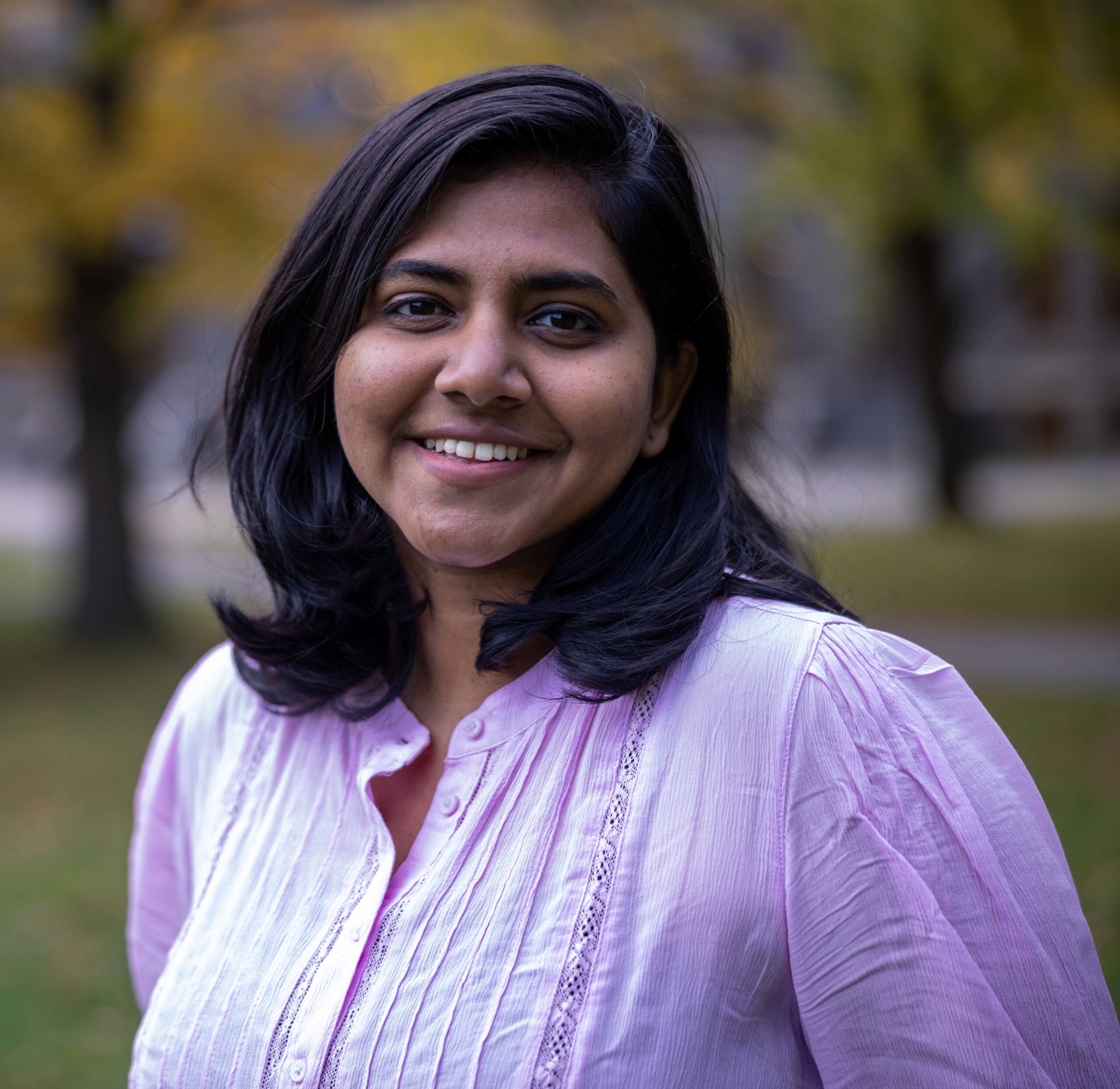 A person with long black hair and a pink button down shirt.